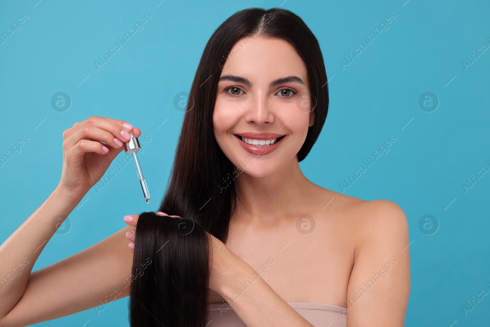 Photo of Beautiful woman applying hair serum on light blue background. Cosmetic product