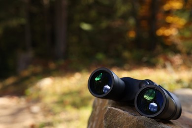 Photo of Binoculars on rock in forest, space for text