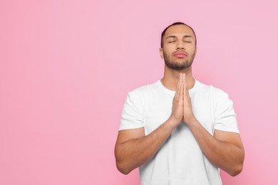 Photo of African American man with clasped hands praying to God on pink background. Space for text