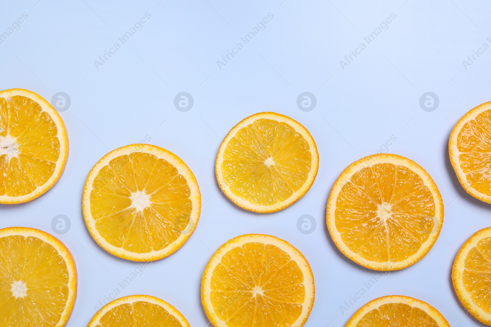 Photo of Slices of juicy orange on light blue background, flat lay. Space for text