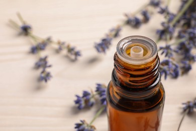 Photo of Bottle of essential oil and lavender flowers on white wooden table, closeup. Space for text