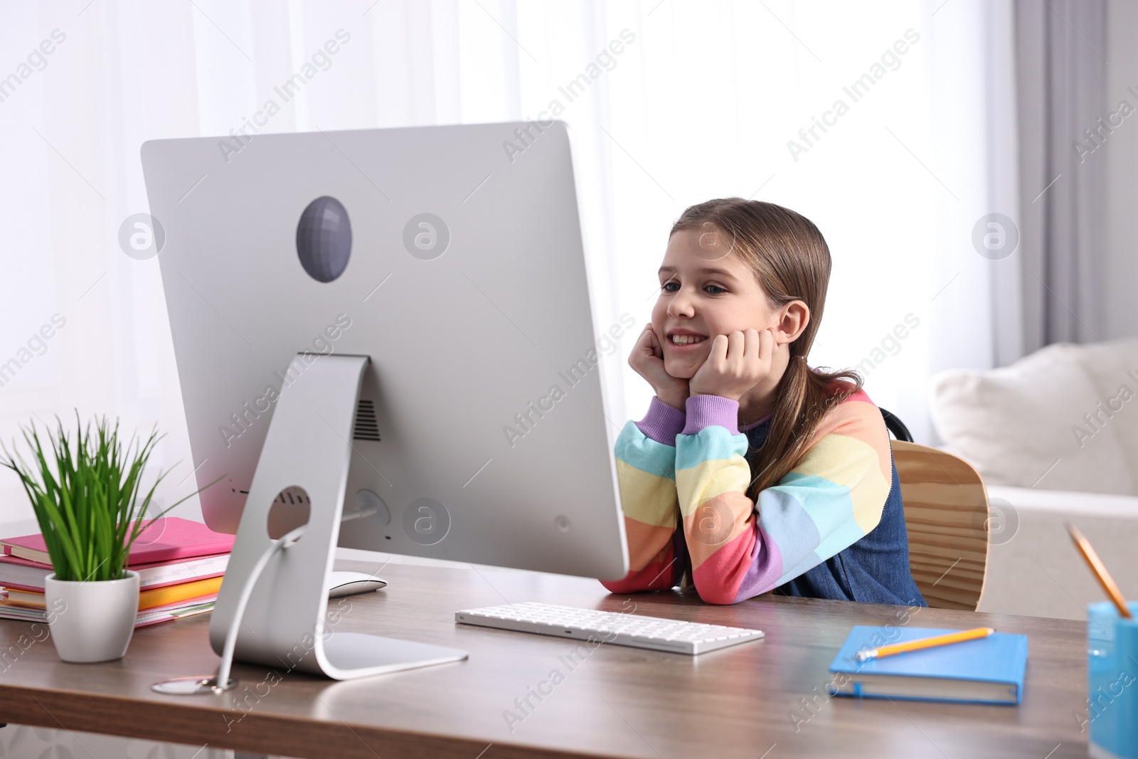 Photo of E-learning. Cute girl using computer during online lesson at table indoors