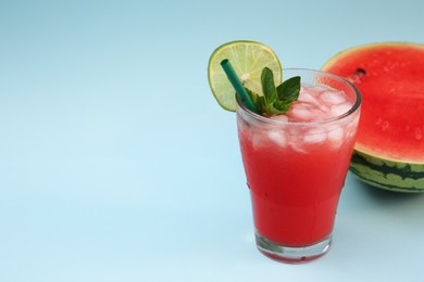 Photo of Glass of delicious drink with lime, ice cubes and cut fresh watermelon on light blue background, space for text