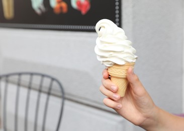 Photo of Woman holding delicious ice cream in wafer cone outdoors, closeup. Space for text