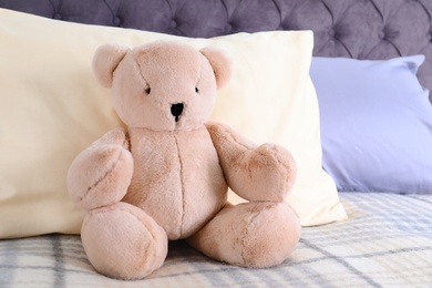 Photo of Cute teddy bear sitting on bed indoors. Space for text