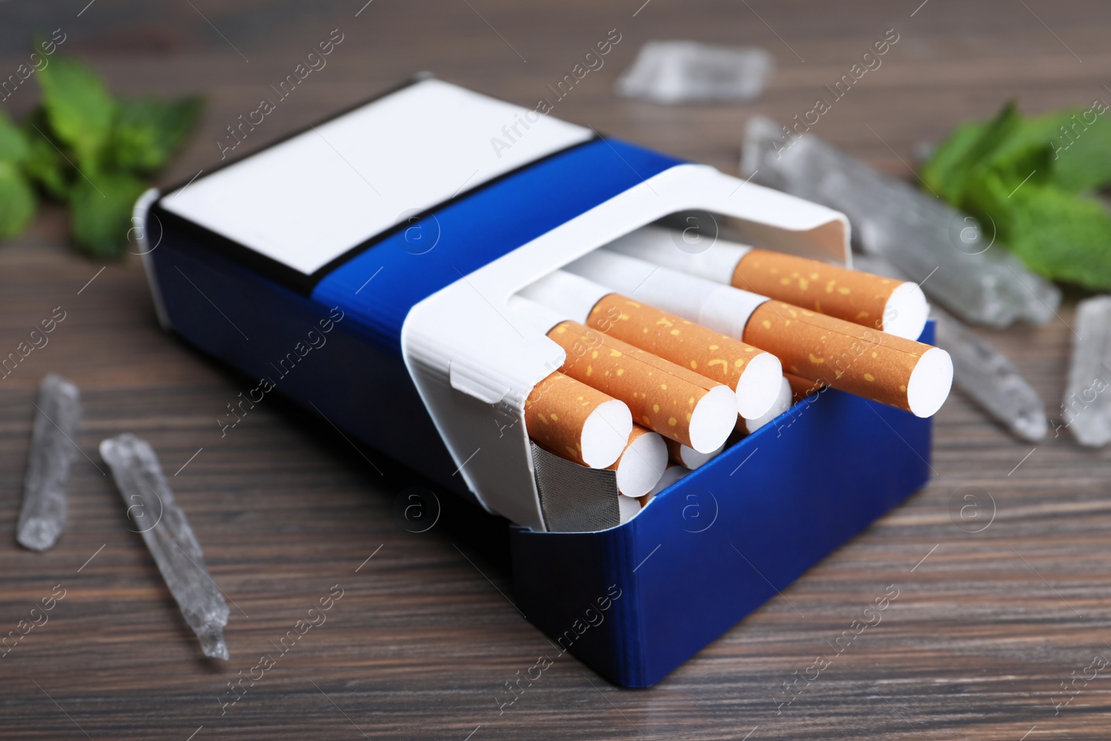 Photo of Pack of cigarettes and menthol crystals on wooden table, closeup