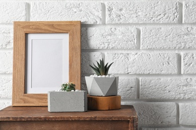 Blank frame and succulent plants on wooden cabinet near white brick wall, space for design. Home decor