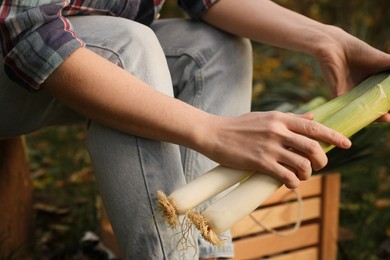 Photo of Woman holding fresh raw leeks outdoors, closeup