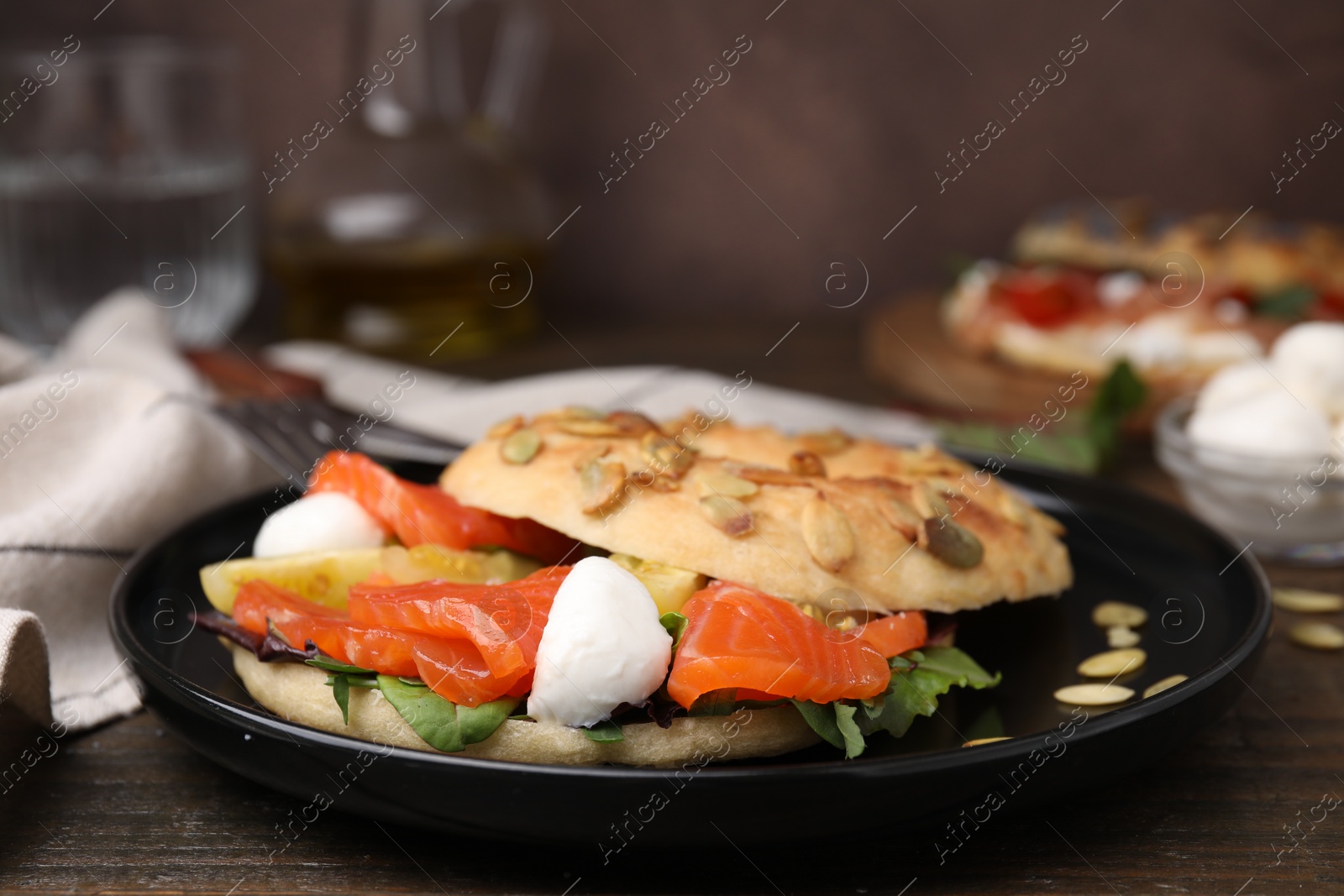 Photo of Tasty bagel with salmon, mozzarella cheese, tomatoes and lettuce on wooden table, closeup