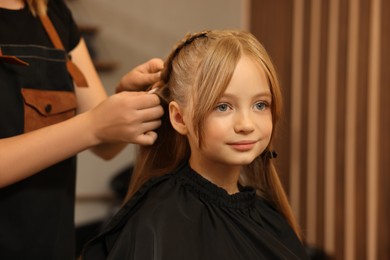 Professional hairdresser braiding girl's hair in beauty salon, closeup