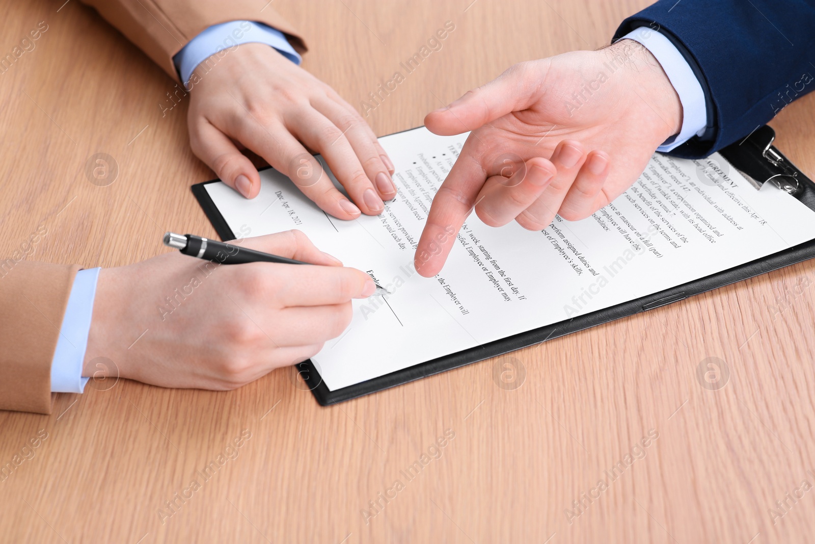 Photo of Businesspeople signing contract at wooden table, closeup of hands