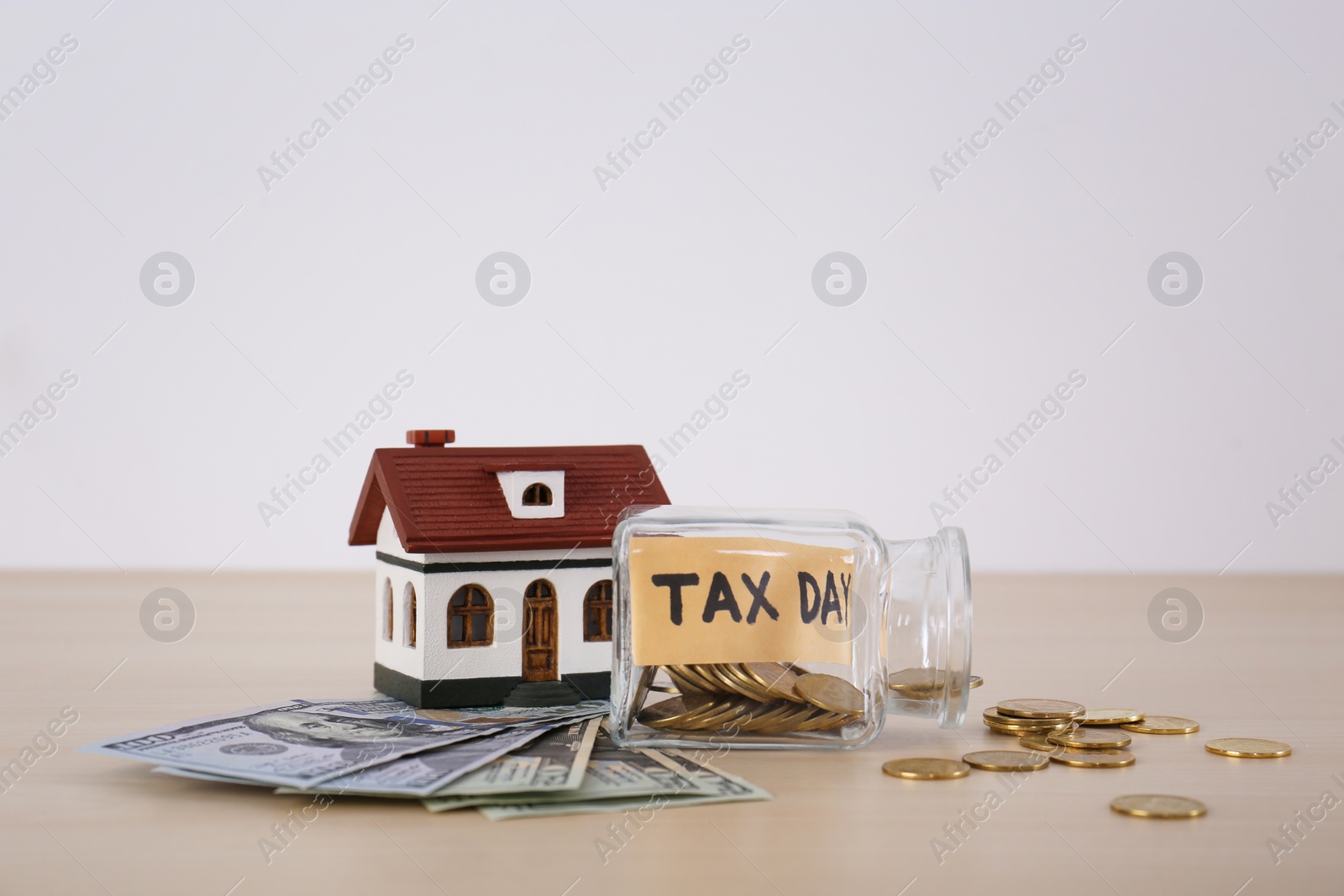 Photo of Glass jar with label "TAX DAY", money and model of house on table