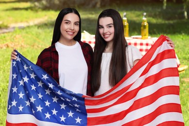Image of 4th of July - Independence day of America. Happy mother and daughter with national flag of United States having picnic in park