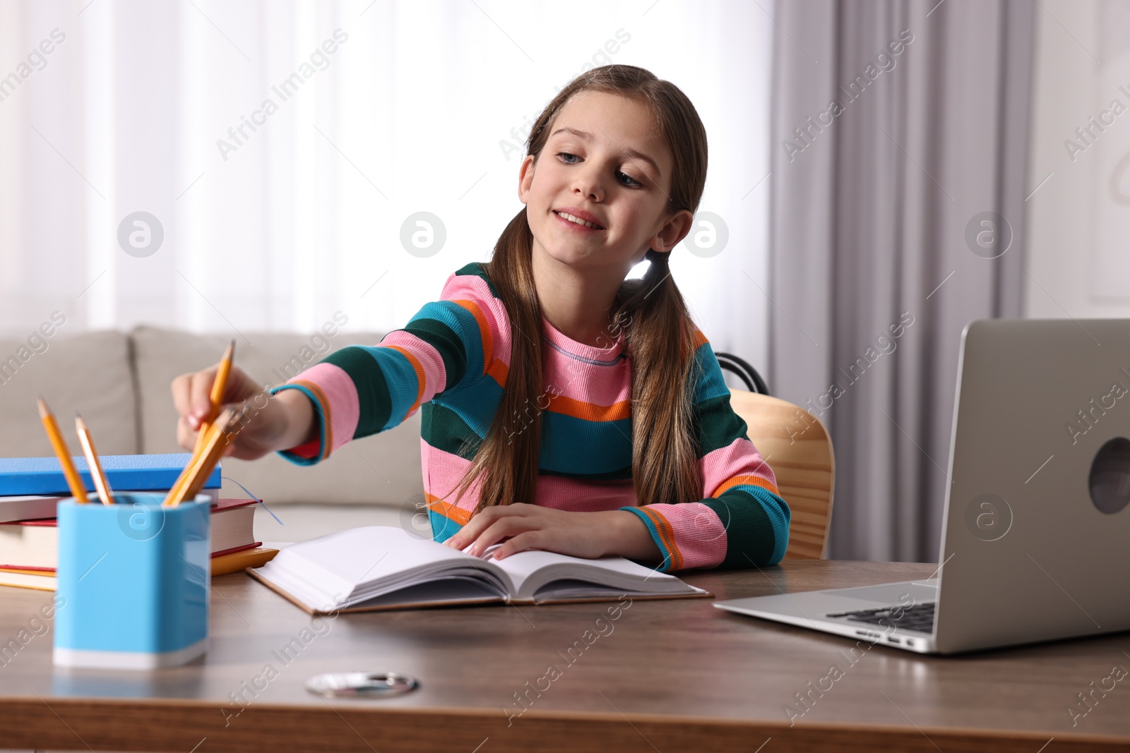 Photo of E-learning. Cute girl using laptop during online lesson at table indoors