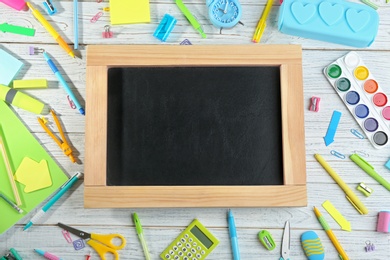 Different school stationery and blank small chalkboard on white wooden background, flat lay. Space for text