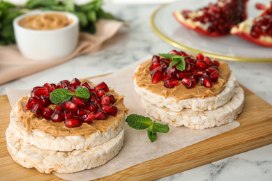 Photo of Puffed rice cakes with peanut butter, pomegranate seeds and mint on table, closeup