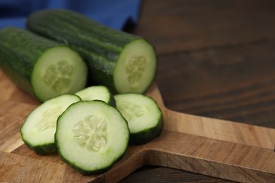 Photo of Fresh whole and cut cucumbers on wooden table, closeup