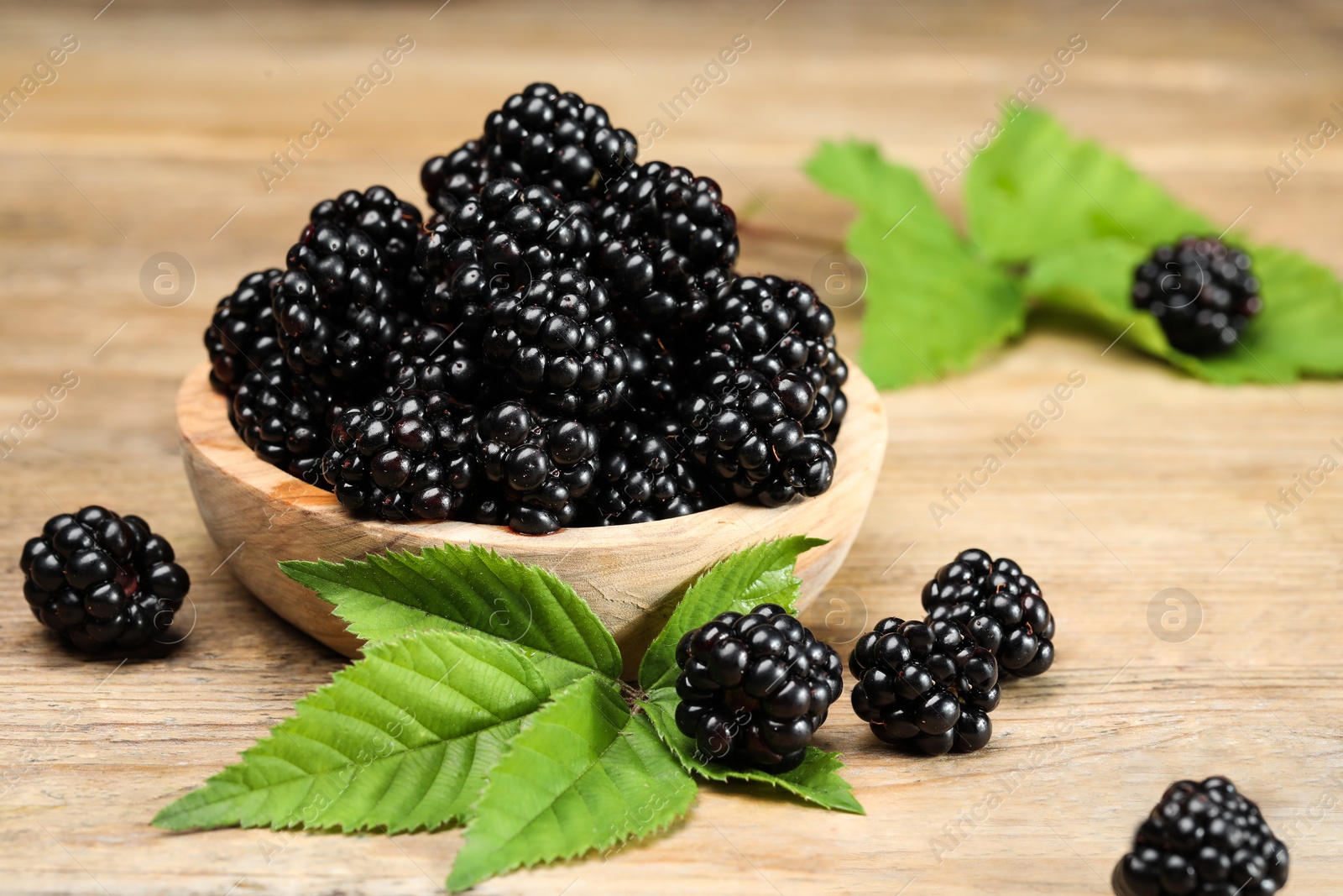Photo of Ripe blackberries and green leaves on wooden table, closeup