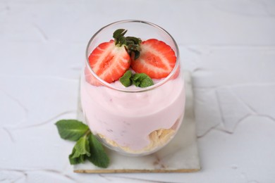 Photo of Glass with yogurt, strawberries and corn flakes on white textured table, closeup