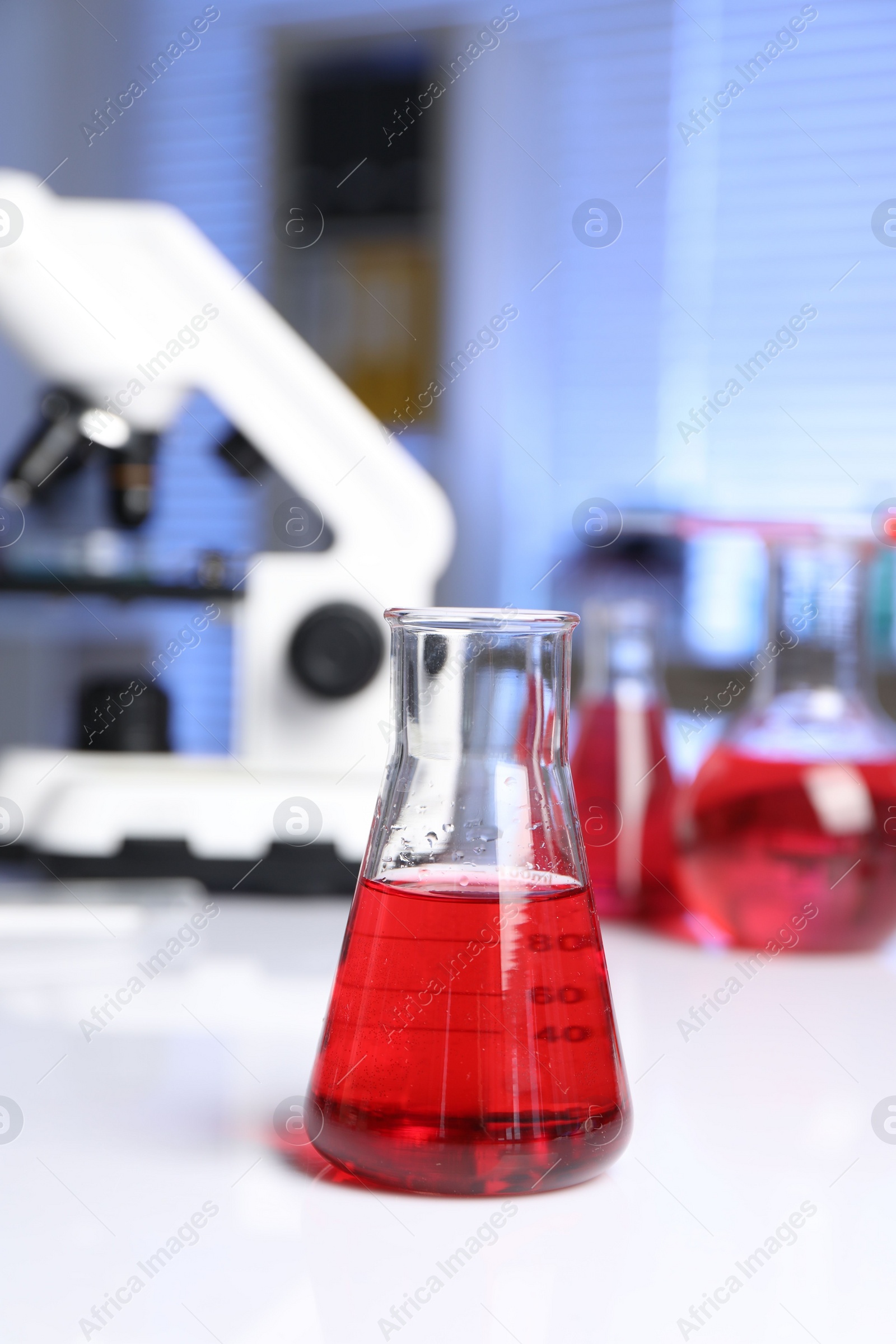 Photo of Laboratory analysis. Glass flask with red liquid and microscope on white table indoors