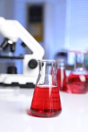 Photo of Laboratory analysis. Glass flask with red liquid and microscope on white table indoors