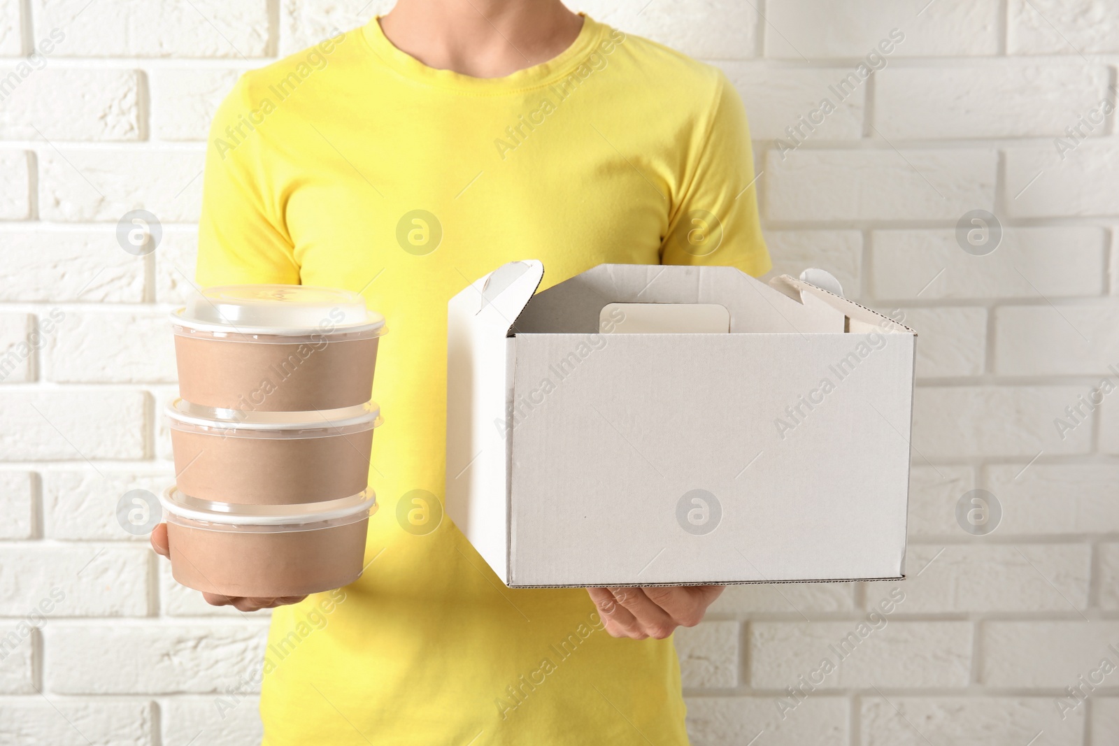 Photo of Courier with different containers near white brick wall, closeup. Food delivery service