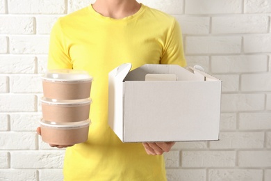 Courier with different containers near white brick wall, closeup. Food delivery service