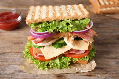 Photo of Tasty sandwich with chicken, ham and bacon  on wooden table