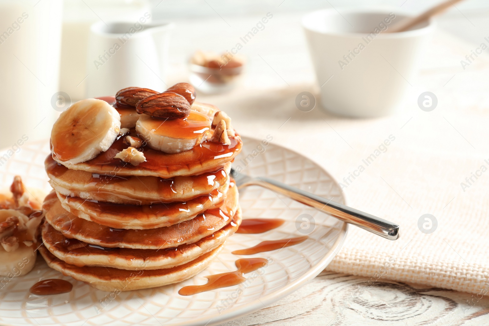 Photo of Stack of tasty pancakes with banana, nuts and syrup on table