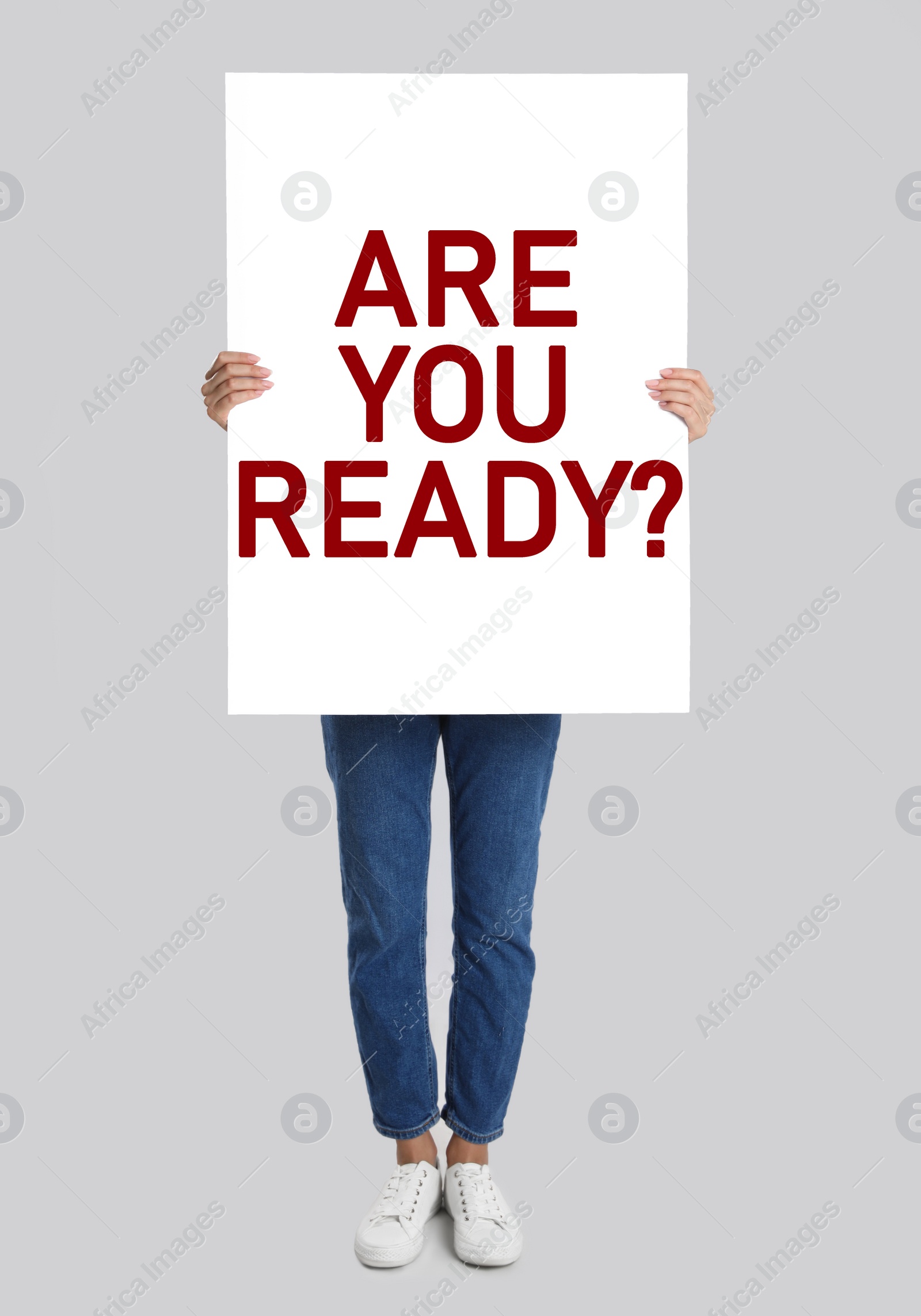 Image of Woman holding poster with text Are You Ready? on light grey background