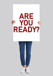 Image of Woman holding poster with text Are You Ready? on light grey background