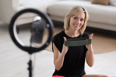 Photo of Smiling sports blogger with with resistance band streaming online fitness lesson at home
