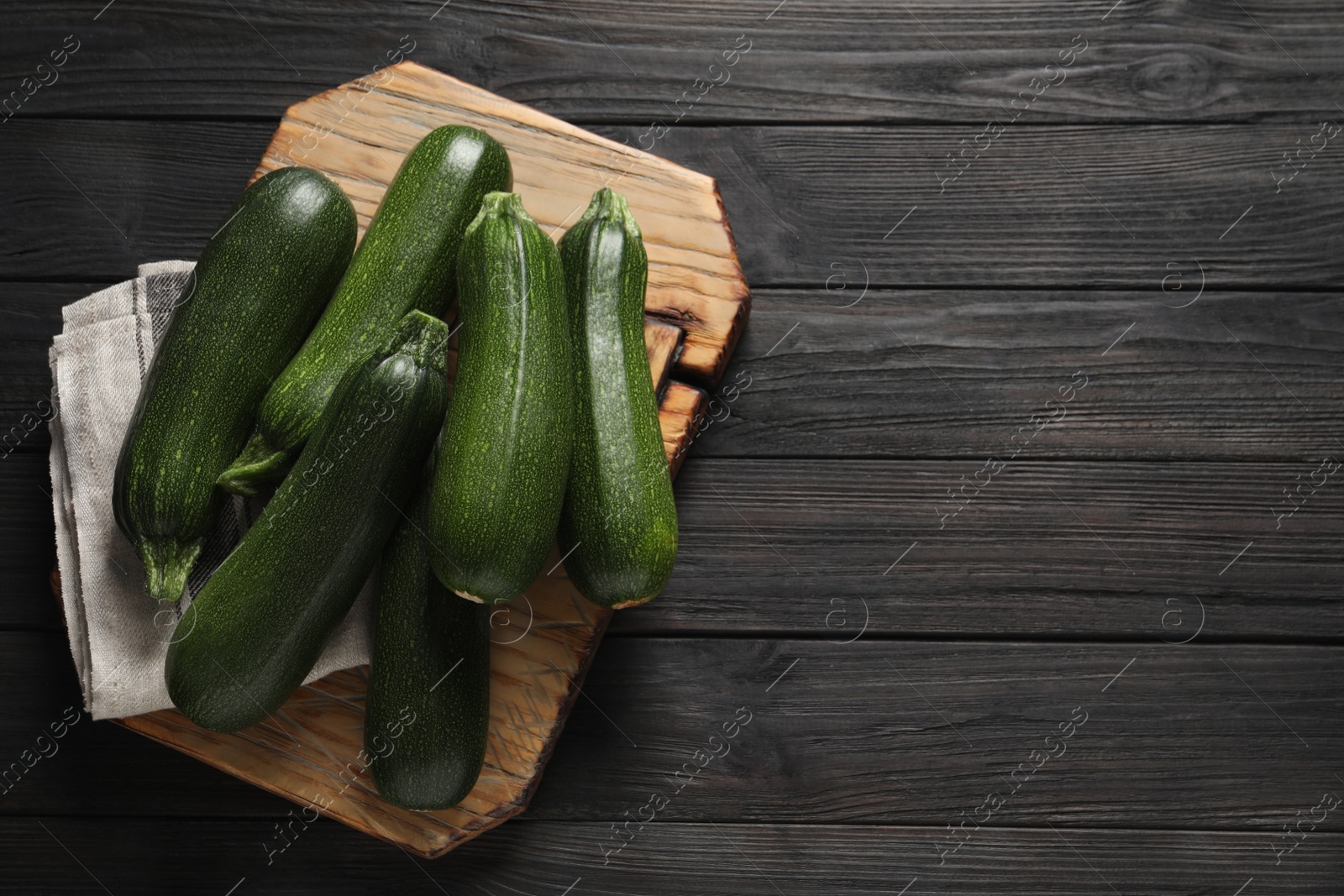 Photo of Raw ripe zucchinis on black wooden table, top view. Space for text