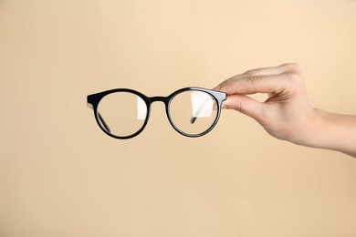 Photo of Woman holding glasses on beige background, closeup. Ophthalmologist prescription