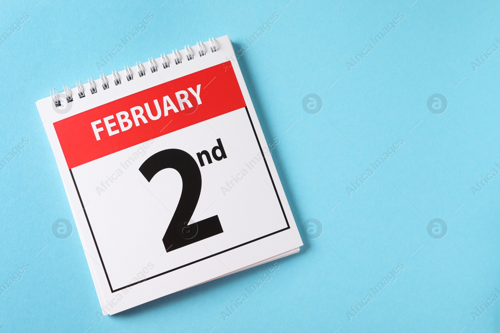 Photo of Top view of calendar with date February 2nd on light blue background, space for text. Groundhog day