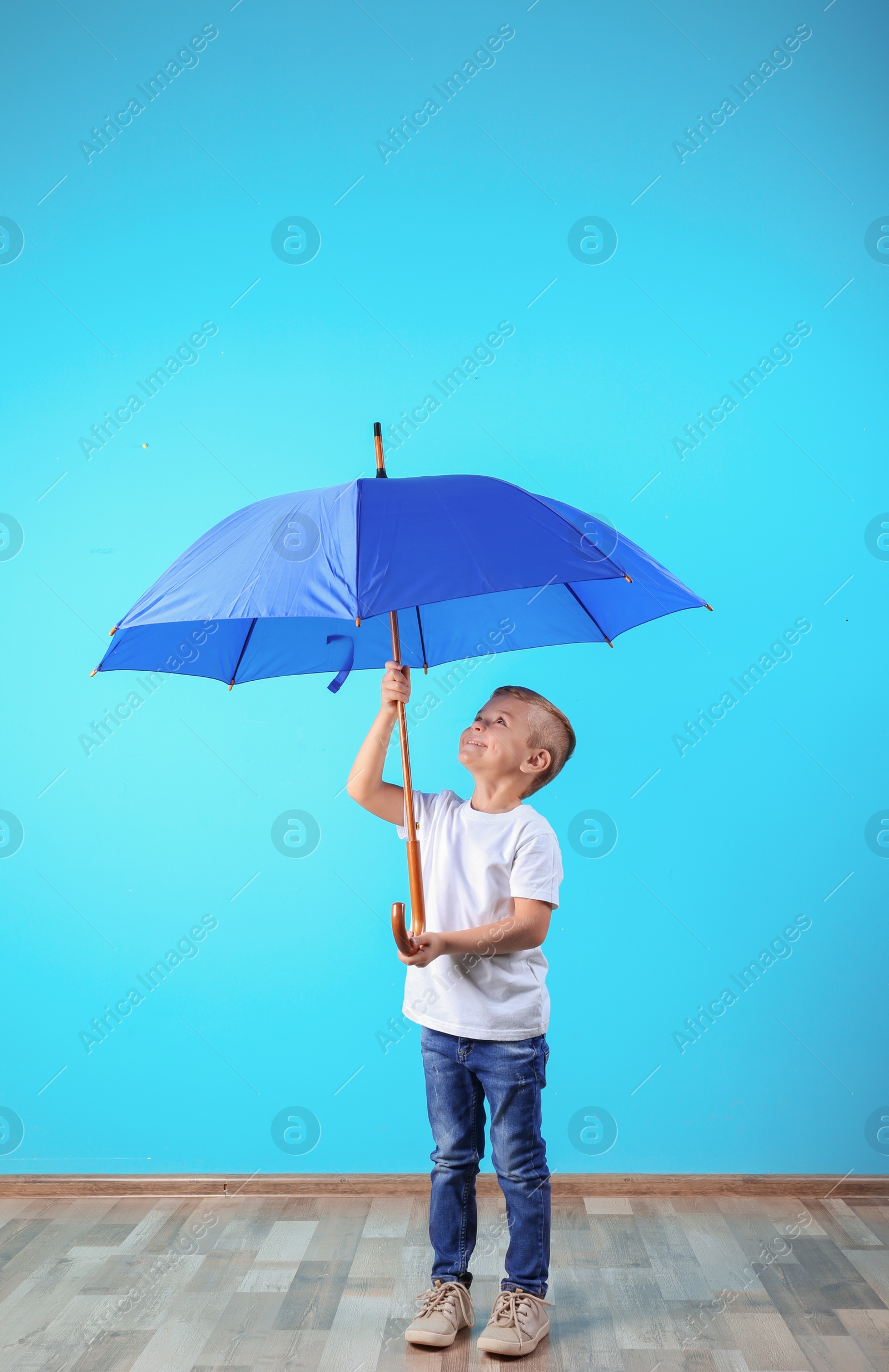 Photo of Little boy with blue umbrella near color wall