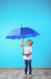 Little boy with blue umbrella near color wall