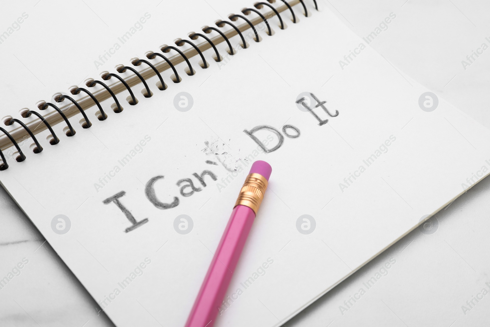 Photo of Motivation concept. Notebook with changed phrase from I Can't Do It into I Can Do It by erasing letter T on white table