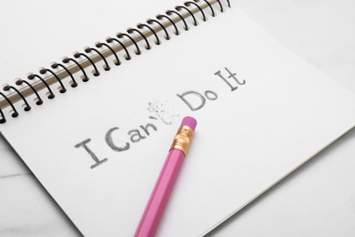 Photo of Motivation concept. Notebook with changed phrase from I Can't Do It into I Can Do It by erasing letter T on white table