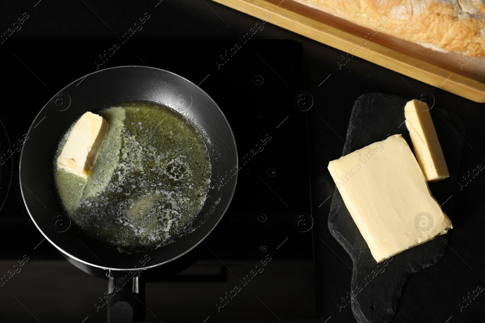 Photo of Melting butter in frying pan and dairy product on black table, top view