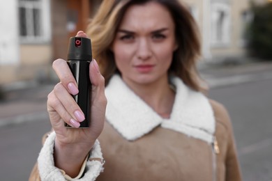 Young woman using pepper spray outdoors, focus on hand