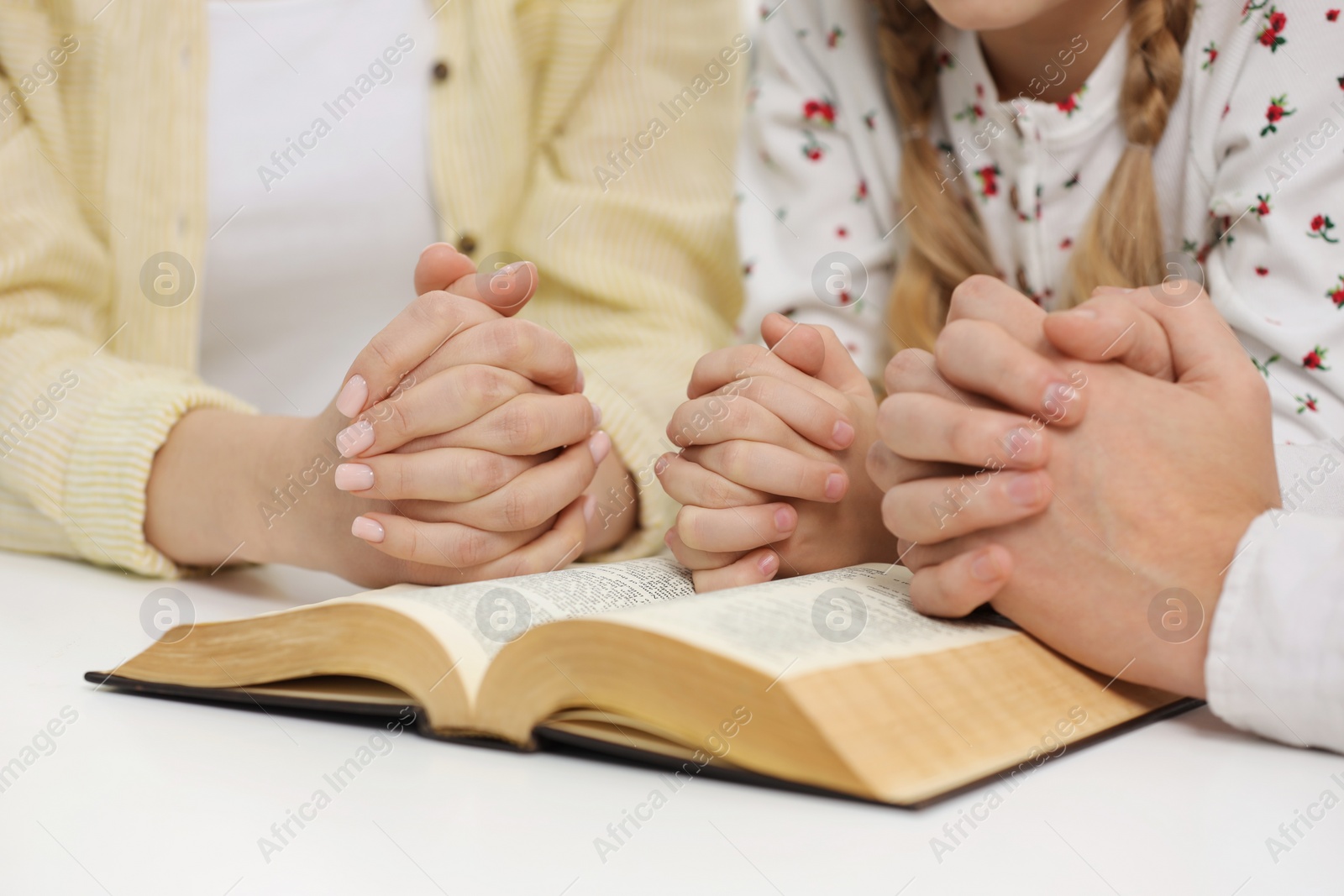 Photo of Girl and her godparents praying over Bible together at table indoors, closeup