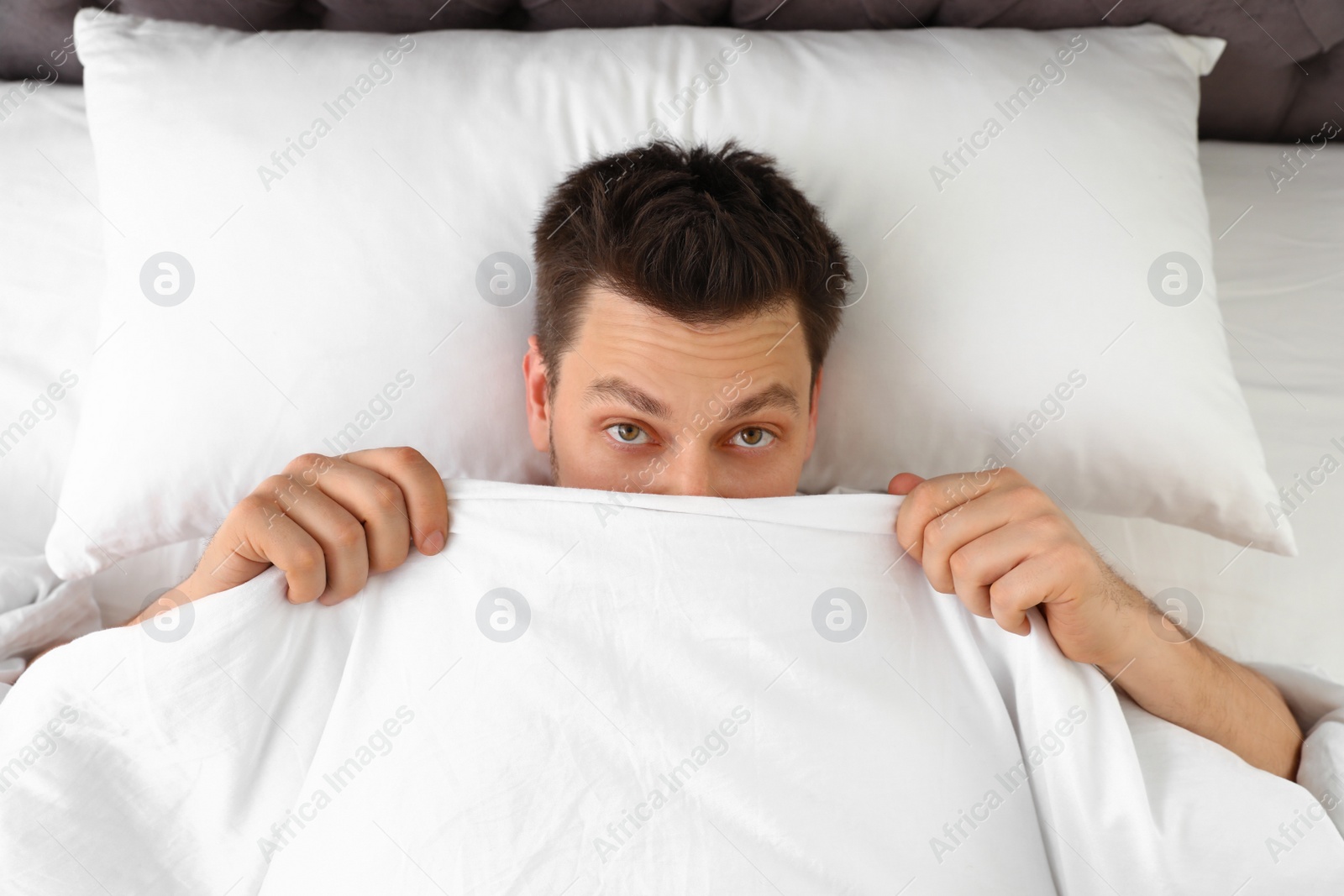 Photo of Handsome man covering his face with blanket while lying on pillow, top view. Bedtime