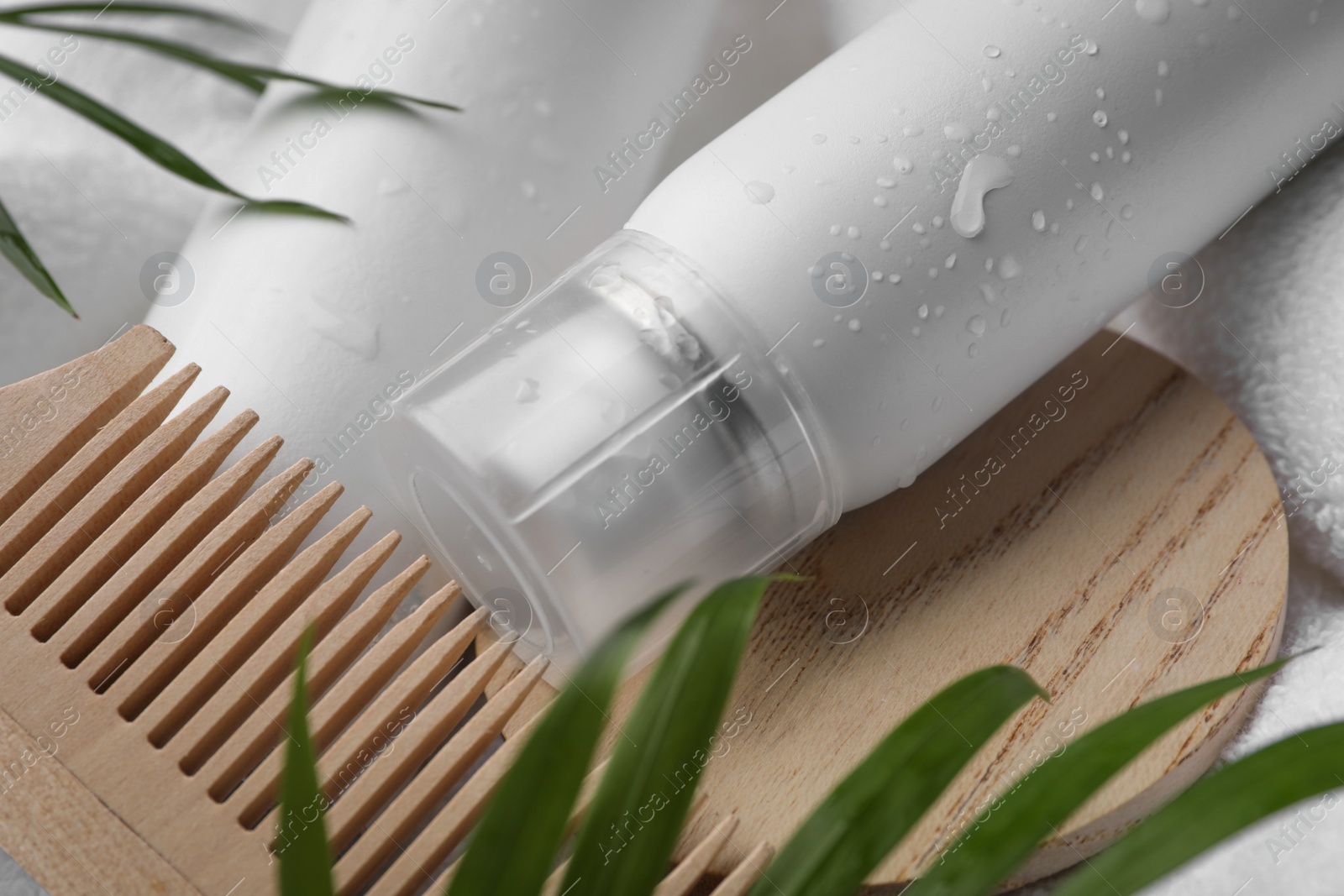 Photo of Wet bottle of dry shampoo spray and wooden comb on white towel, closeup