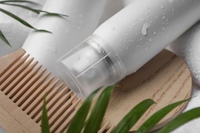 Photo of Wet bottle of dry shampoo spray and wooden comb on white towel, closeup