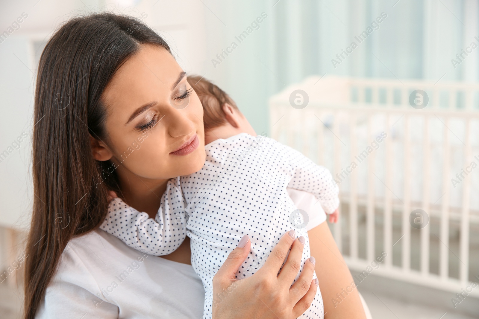 Photo of Woman holding her baby in light nursery. Space for text