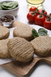 Photo of Raw vegan cutlets and different products on white table, closeup