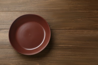 Photo of Clean brown plate on wooden table, top view. Space for text