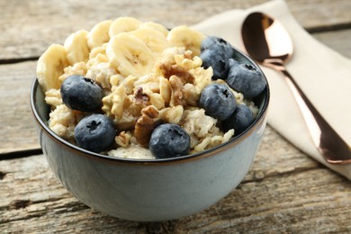 Photo of Tasty oatmeal with banana, blueberries and walnuts served in bowl on wooden table, closeup