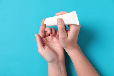 Woman applying cosmetic cream from tube onto her hand on light blue background, top view